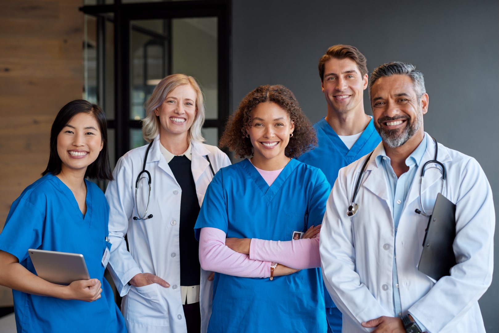 Team of healthcare professionals in scrubs and lab coats standing together in a hospital or clinic environment.