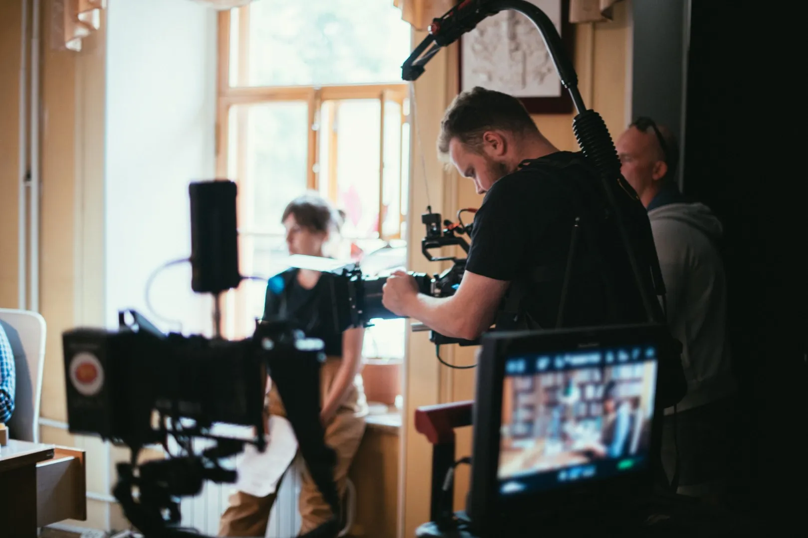 Camera operator filming a scene indoors with professional video equipment and monitors.