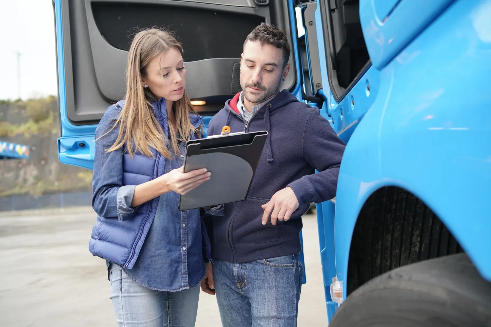 Two transportation professionals standing beside a blue semi-truck reviewing information on a Paper Pad.