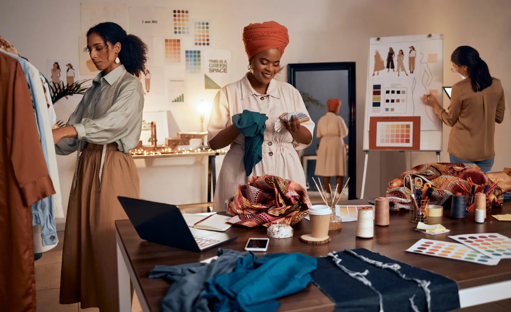 Small business owners working in a creative studio with fabrics, sewing materials, and design sketches spread across a table.