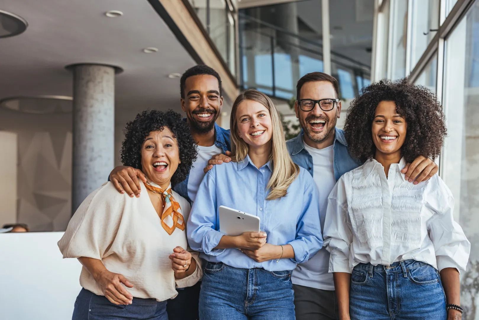 Group of colleagues standing together in an office environment, smiling and posing for a team photo with relaxed, friendly body language