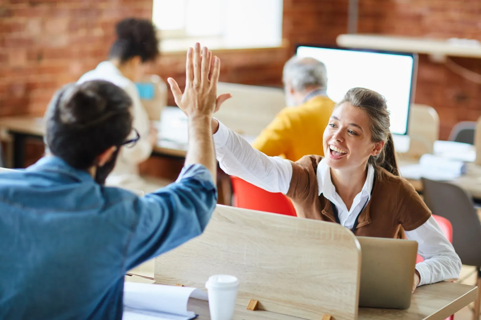Two coworkers sharing a high-five in a collaborative office environment, celebrating teamwork and a positive workplace moment