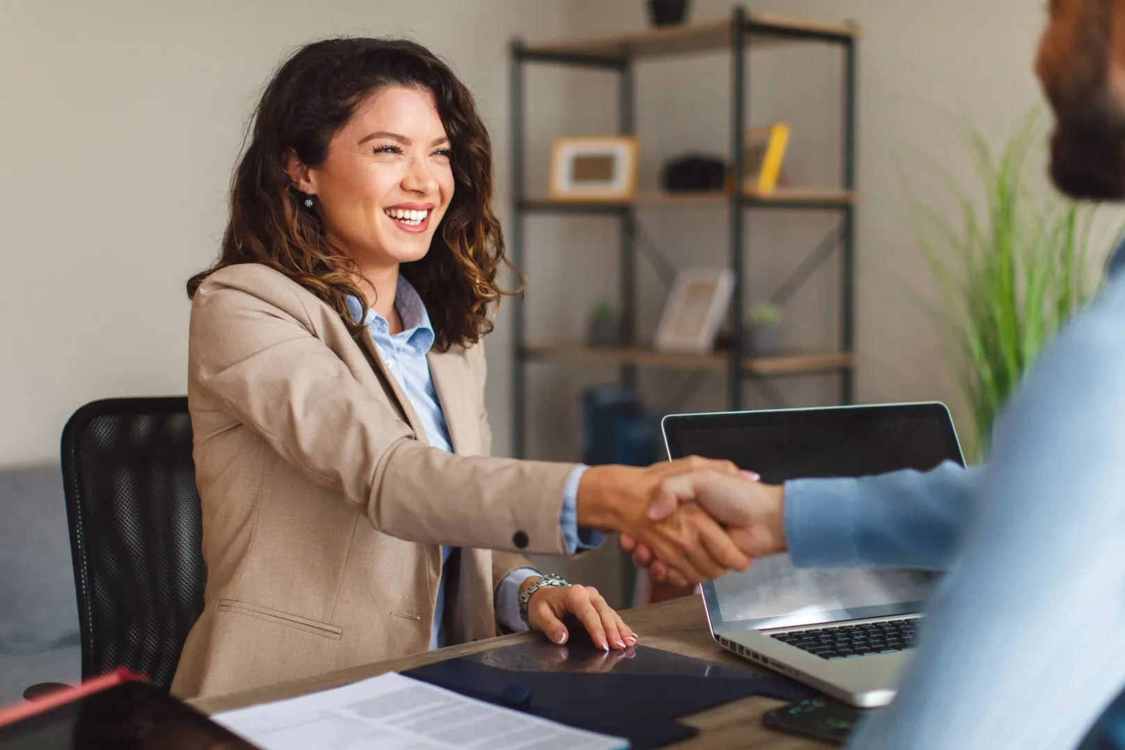 Candidate and interviewer shaking hands across a desk in an office setting, representing job opportunities and the start of a new professional role