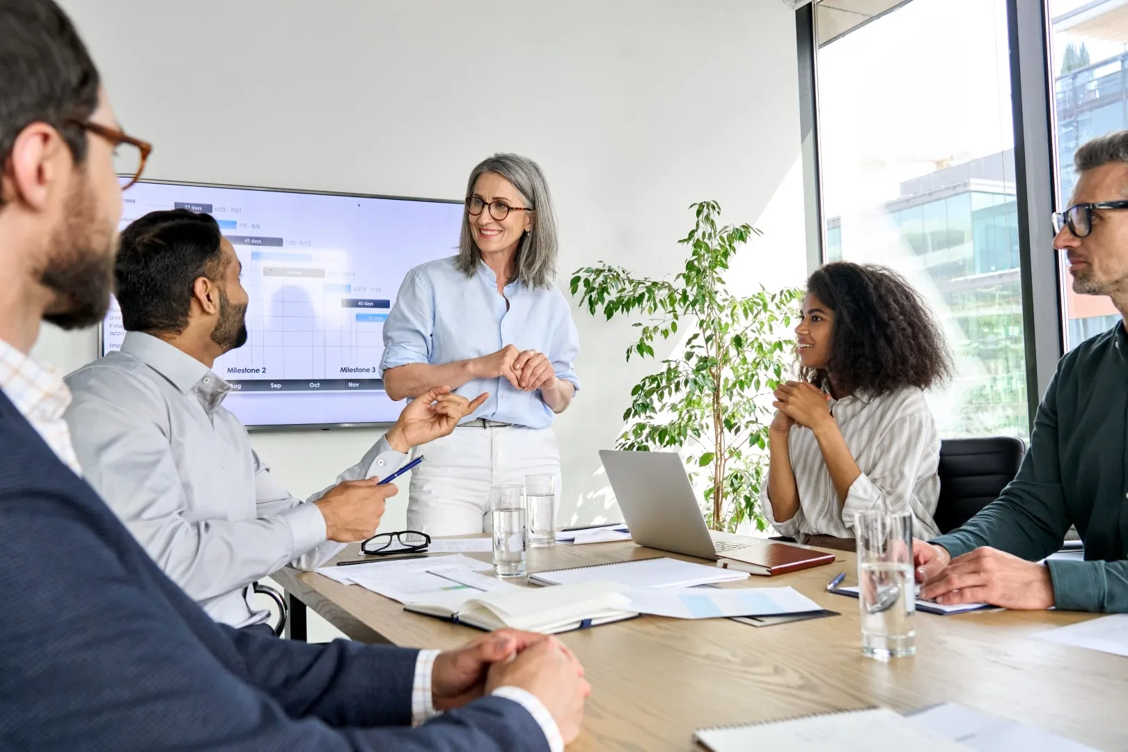 Team engaged in a meeting around a conference table while a presenter stands and leads a discussion