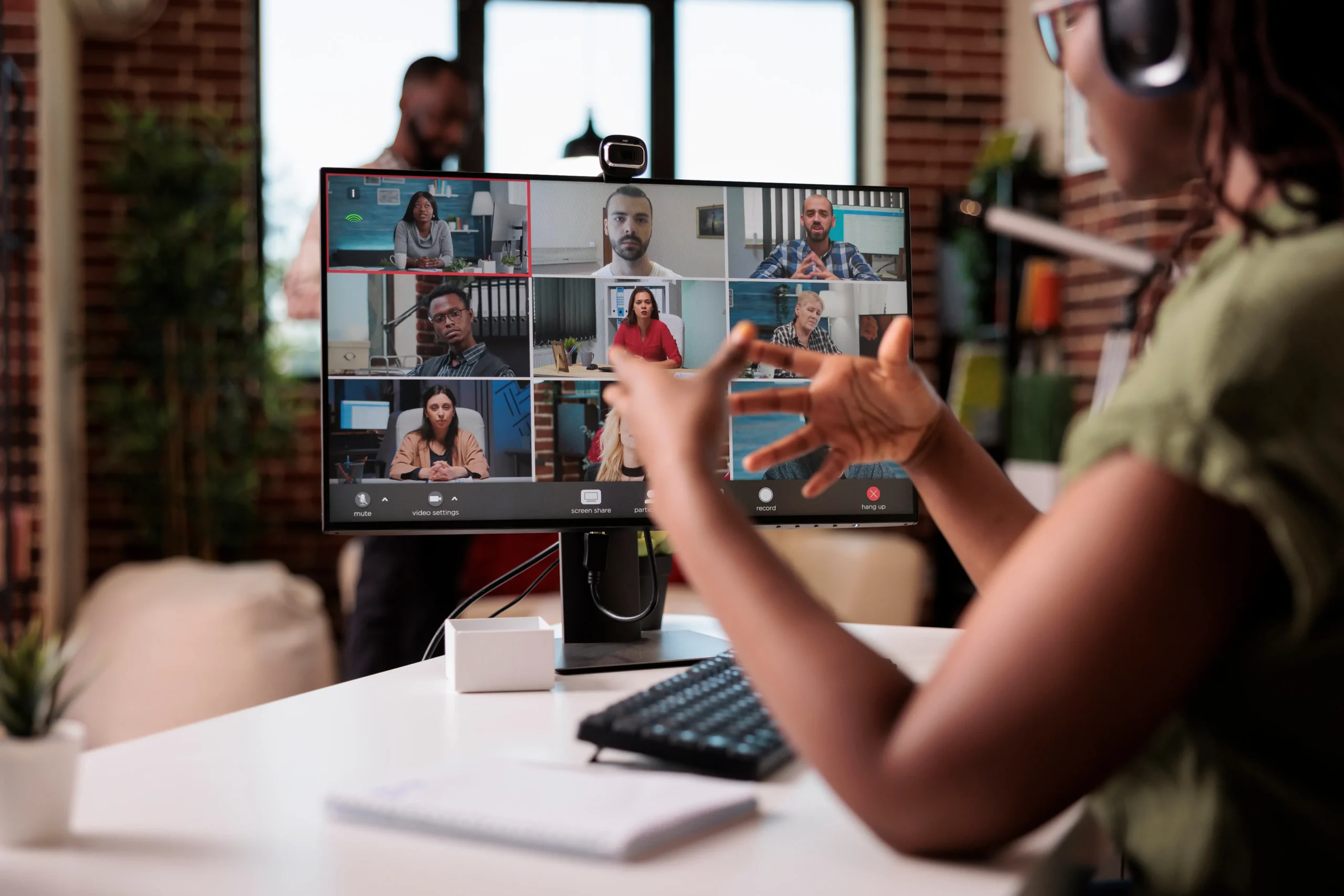 Person participating in an online webinar, speaking while viewing a screen displaying multiple attendees in a virtual meeting grid.